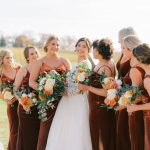 Bride and bridesmaids in rust-colored velvet dresses with coordinated updo hairstyles holding fall-colored bouquets
