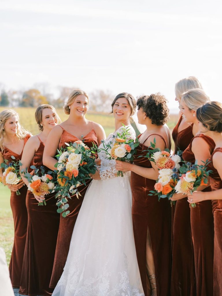 Bride and bridesmaids in rust-colored velvet dresses with coordinated updo hairstyles holding fall-colored bouquets