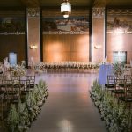 Grand ballroom ceremony with Art Deco details, gold chiavari chairs, and white floral aisle arrangements