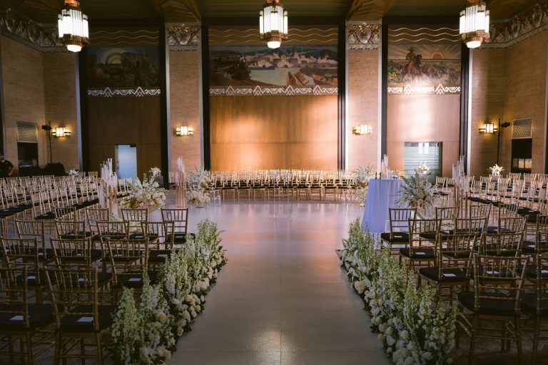 Grand ballroom ceremony with Art Deco details, gold chiavari chairs, and white floral aisle arrangements