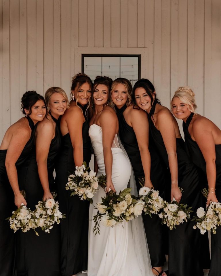 Bride and bridesmaids in coordinated black dresses holding white bouquets