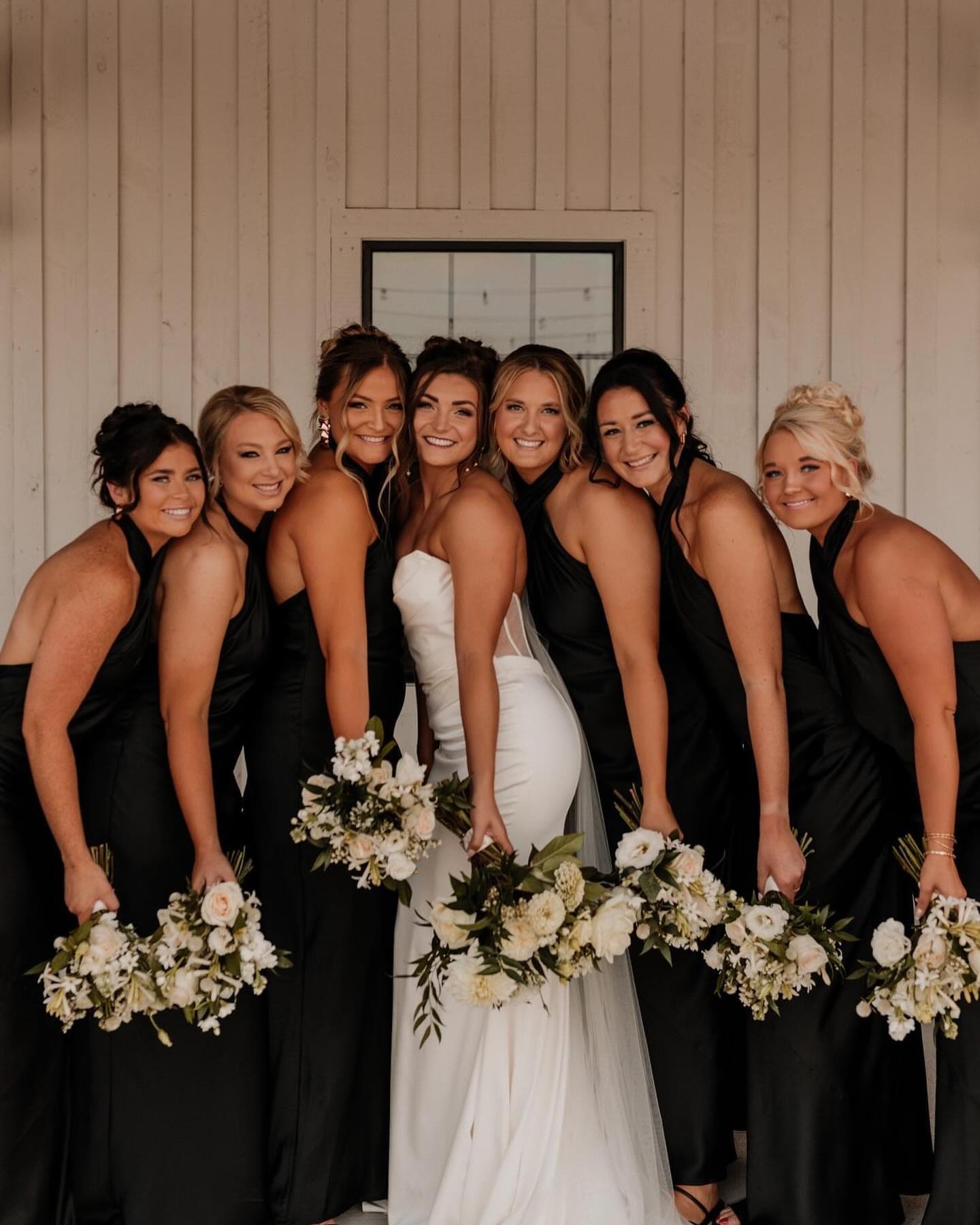 Bride and bridesmaids in coordinated black dresses holding white bouquets