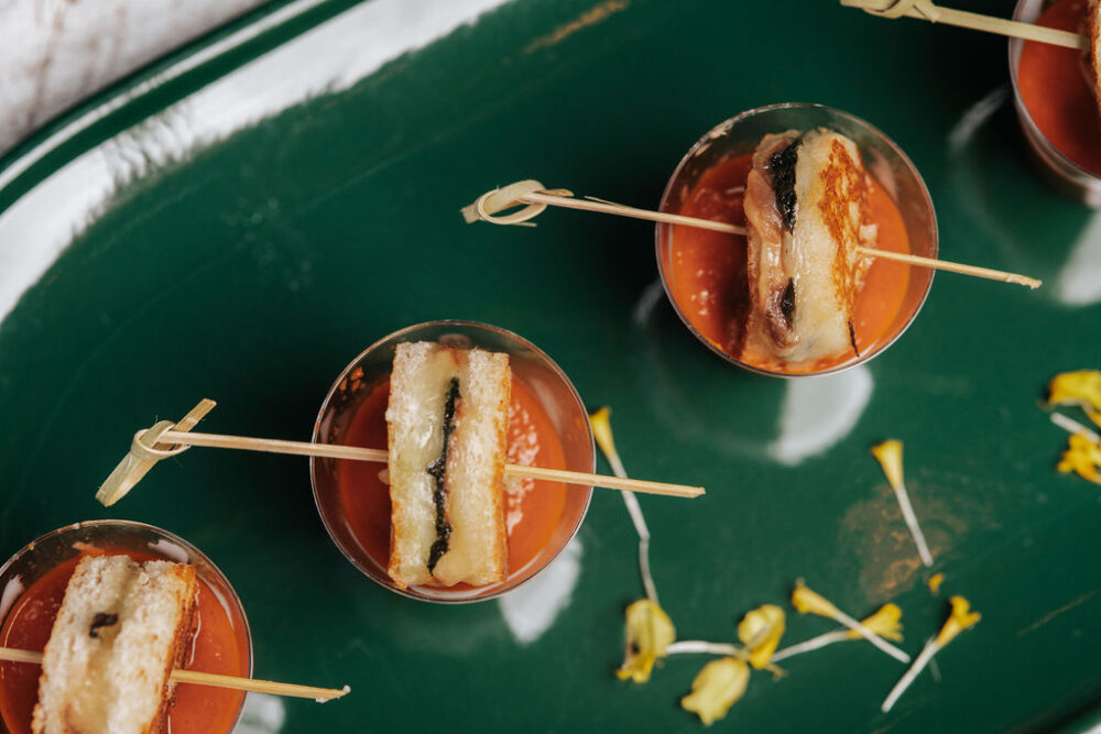 Grilled cheese sandwich bites served on wooden skewers in copper cocktail glasses