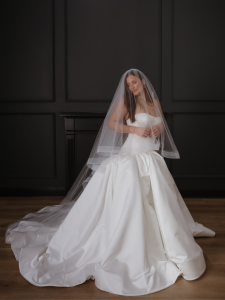 Bride in elegant ball gown wedding dress with cathedral veil seated in dark-paneled room
