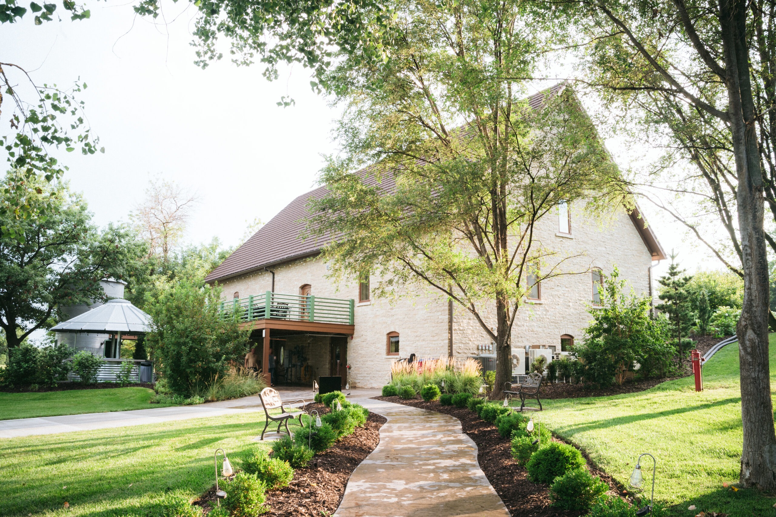 Rustic Nebraska barn wedding venue with curved walkway through manicured gardens and mature trees