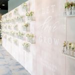 Wedding escort card display wall in soft blush tones with rows of bud vases and romantic calligraphy signage