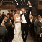 Newlyweds celebrate reception entrance in rustic barn with string lights