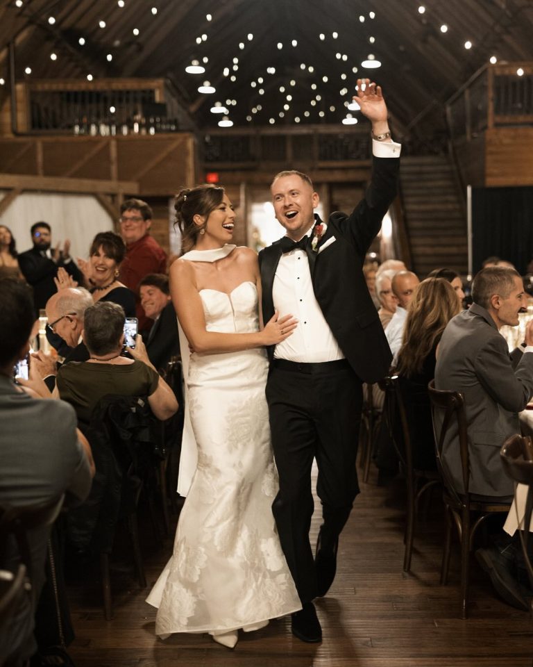 Newlyweds celebrate reception entrance in rustic barn with string lights