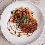 Seared chicken breast with colorful vegetable medley and microgreens garnish on white plate with balsamic drizzle