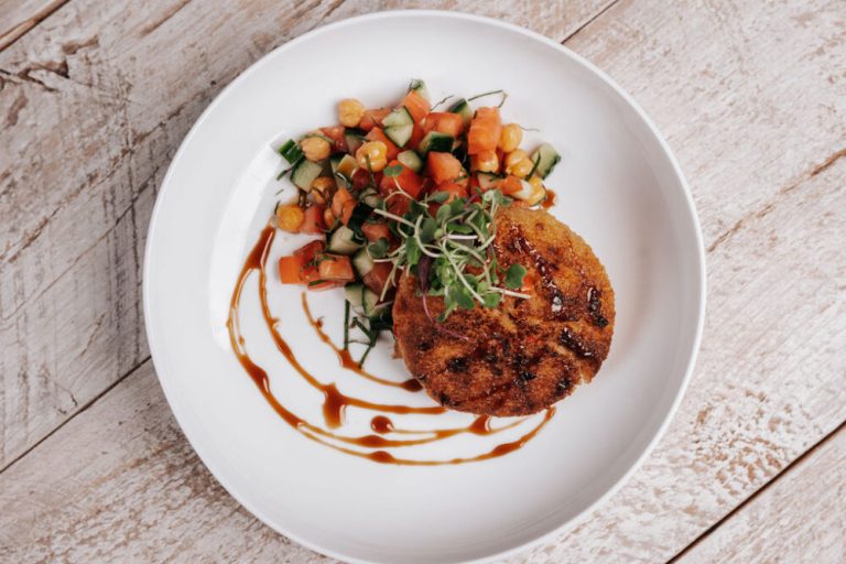 Seared chicken breast with colorful vegetable medley and microgreens garnish on white plate with balsamic drizzle