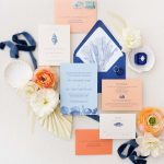 Nautical wedding invitation suite in navy and coral with seashell envelope liner, blue ribbon, and white and peach florals