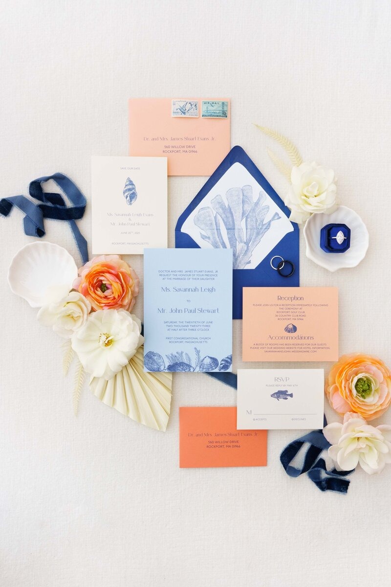 Nautical wedding invitation suite in navy and coral with seashell envelope liner, blue ribbon, and white and peach florals