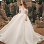 Bride in classic ball gown wedding dress with off-shoulder sleeves and flowing train at historic stone estate