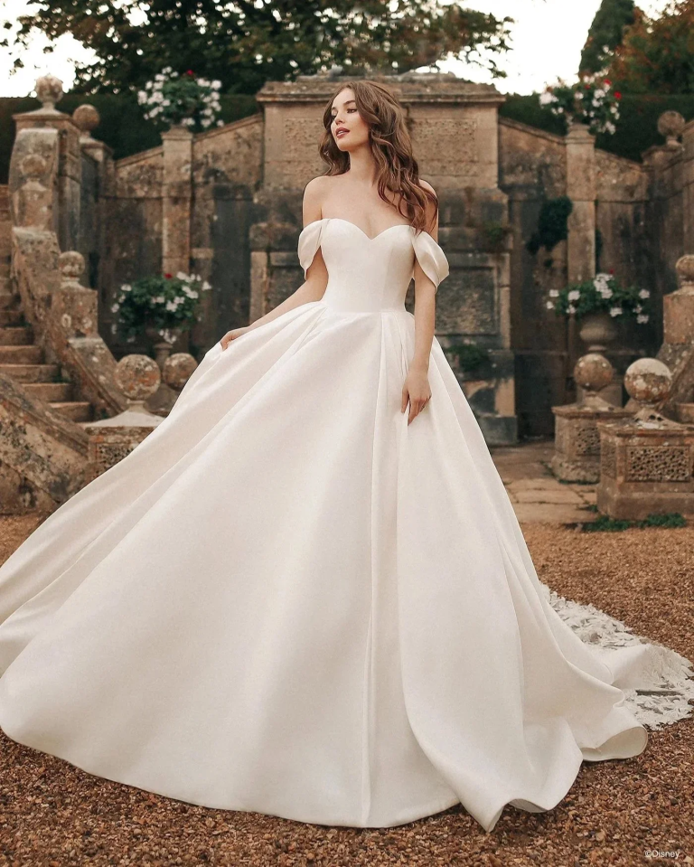 Bride in classic ball gown wedding dress with off-shoulder sleeves and flowing train at historic stone estate