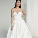 Model in strapless ball gown wedding dress with fitted bodice and full skirt, accessorized with pearl jewelry