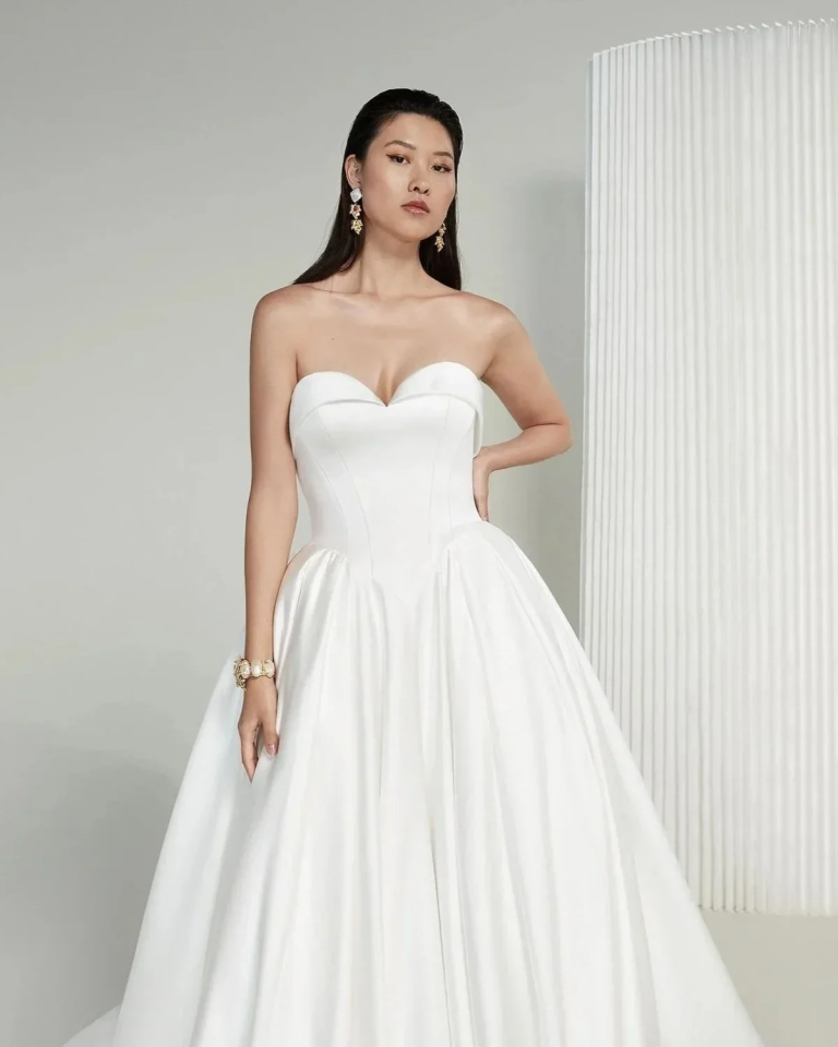 Model in strapless ball gown wedding dress with fitted bodice and full skirt, accessorized with pearl jewelry