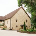Historic limestone barn exterior with peaked gable roof, arched wooden doors, and landscaped entrance