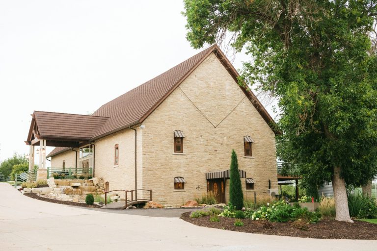 Historic limestone barn exterior with peaked gable roof, arched wooden doors, and landscaped entrance