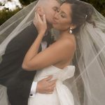 Couple embraces under flowing veil in romantic outdoor wedding moment