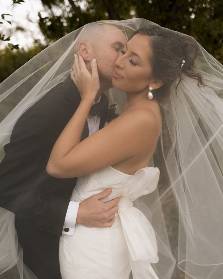 Couple embraces under flowing veil in romantic outdoor wedding moment