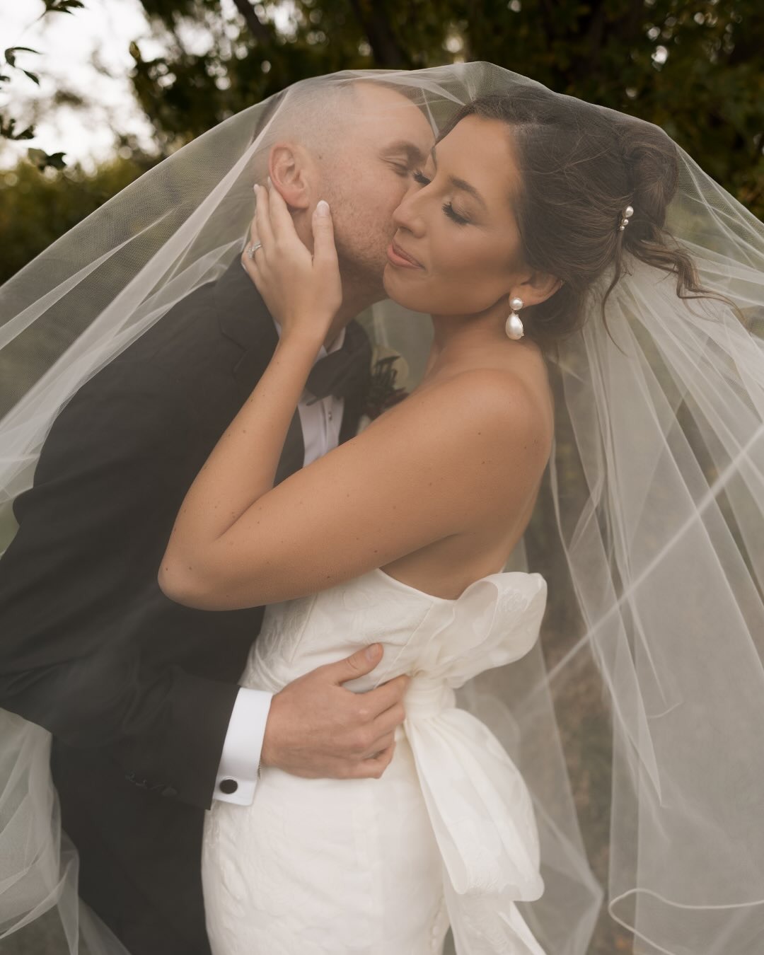 Couple embraces under flowing veil in romantic outdoor wedding moment