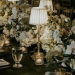 Opulent wedding reception table with brass lamp centerpieces, white hydrangeas, roses, and mercury glass candle holders
