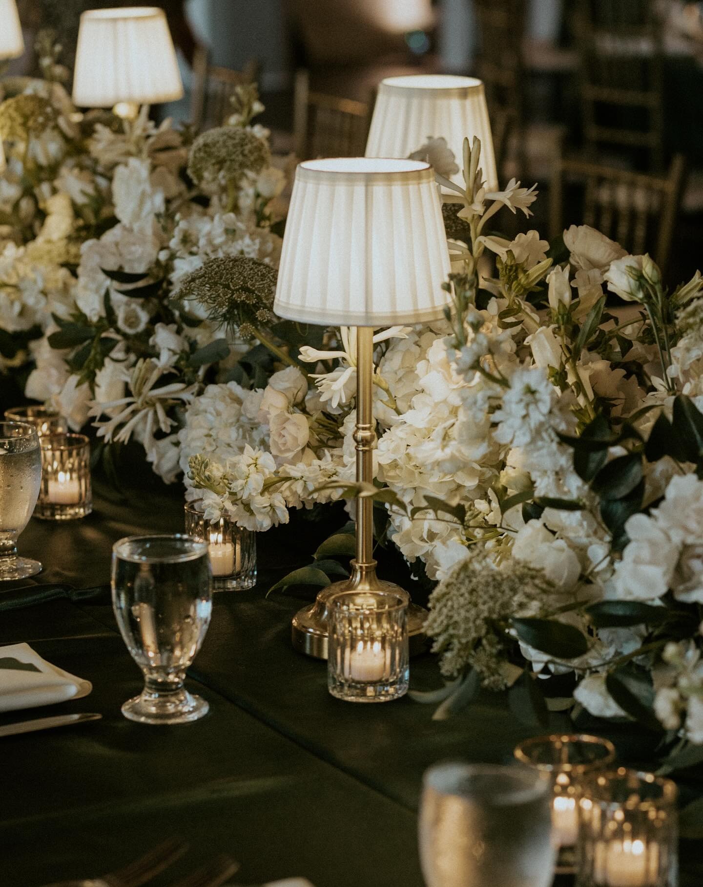 Opulent wedding reception table with brass lamp centerpieces, white hydrangeas, roses, and mercury glass candle holders