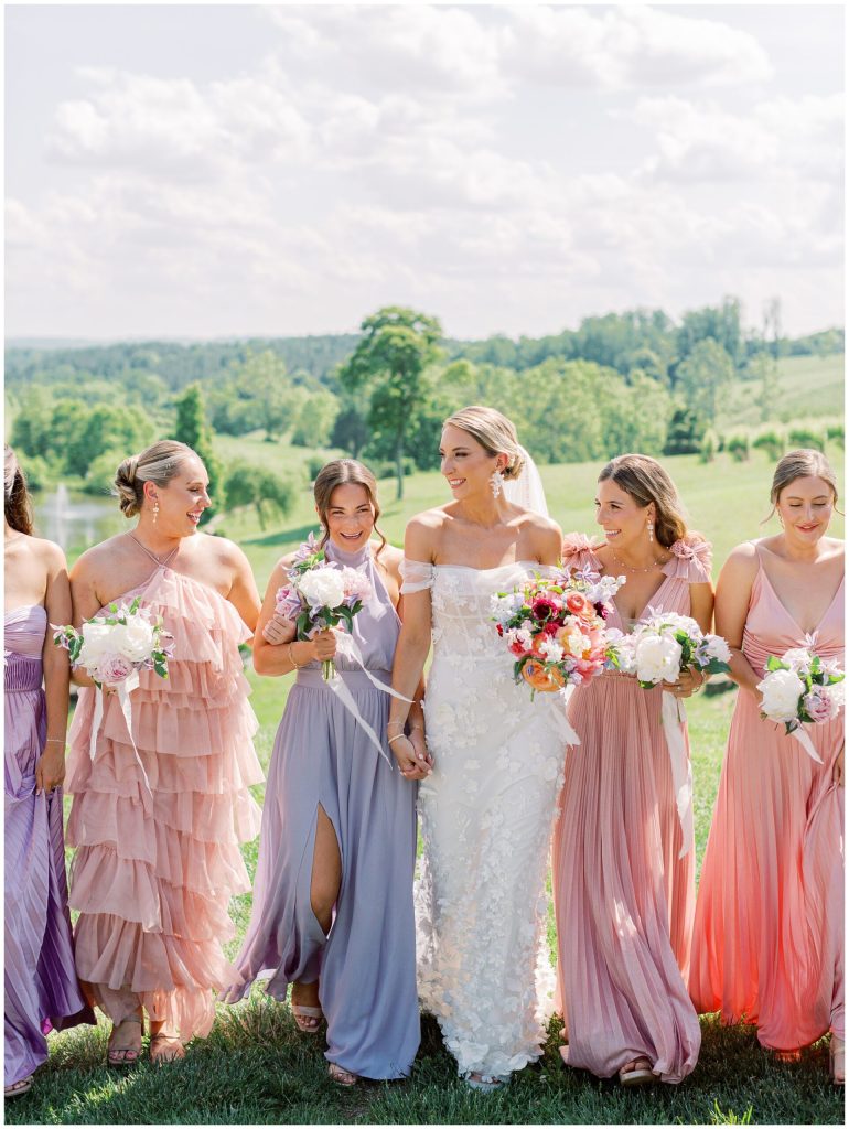 Bride and bridesmaids in pastel pink and lavender dresses walking together outdoors at Northern Virginia vineyard