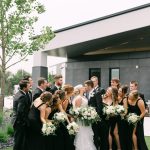 Wedding party gathered around bride and groom at contemporary venue with modern architecture and green lawn