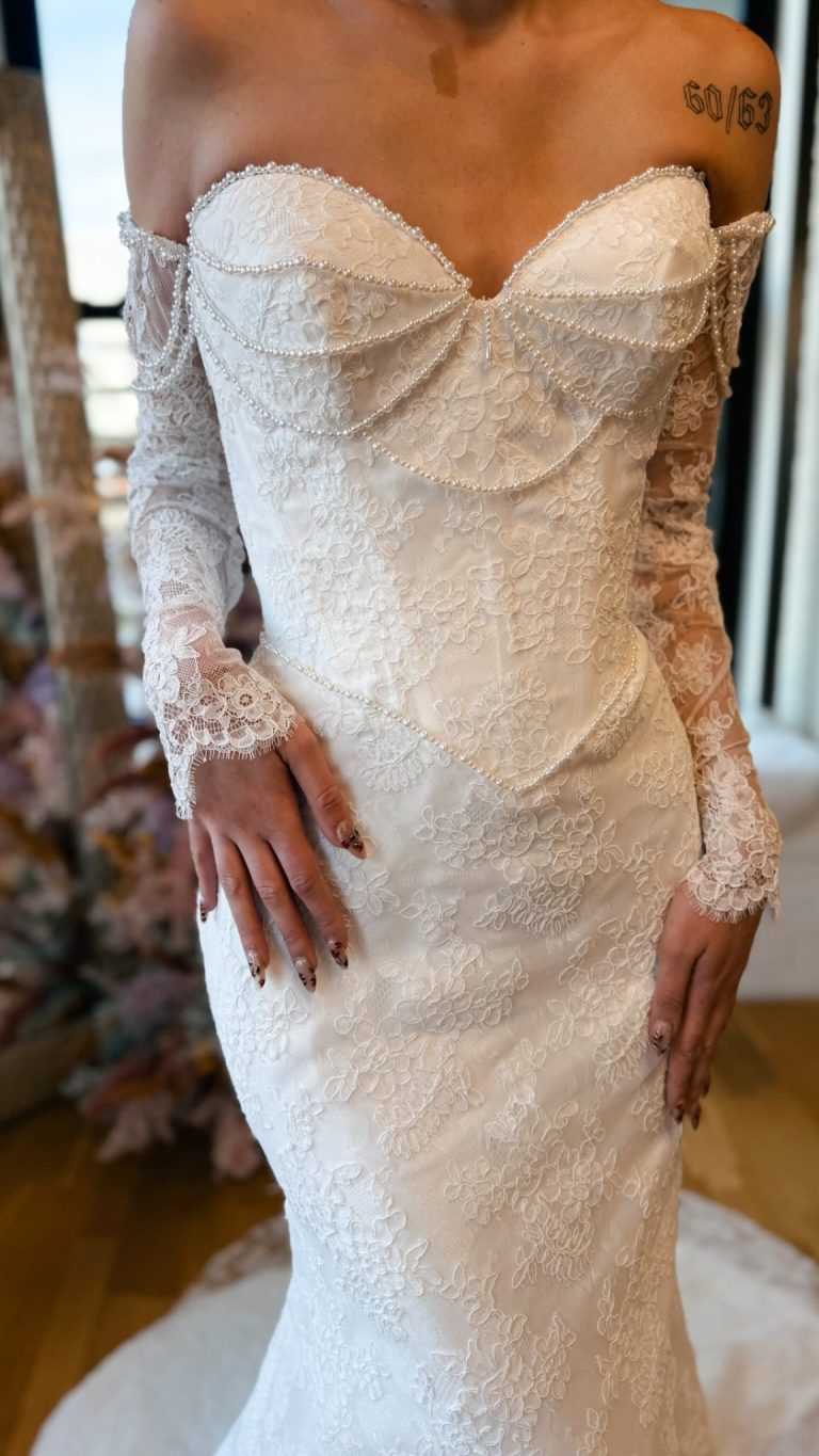 Ivory lace wedding dress with off-shoulder neckline, pearl-trimmed corset bodice, and fitted mermaid skirt with floral embroidery