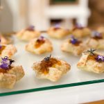 Gourmet canapés with jam and edible flower garnishes arranged on glass platter