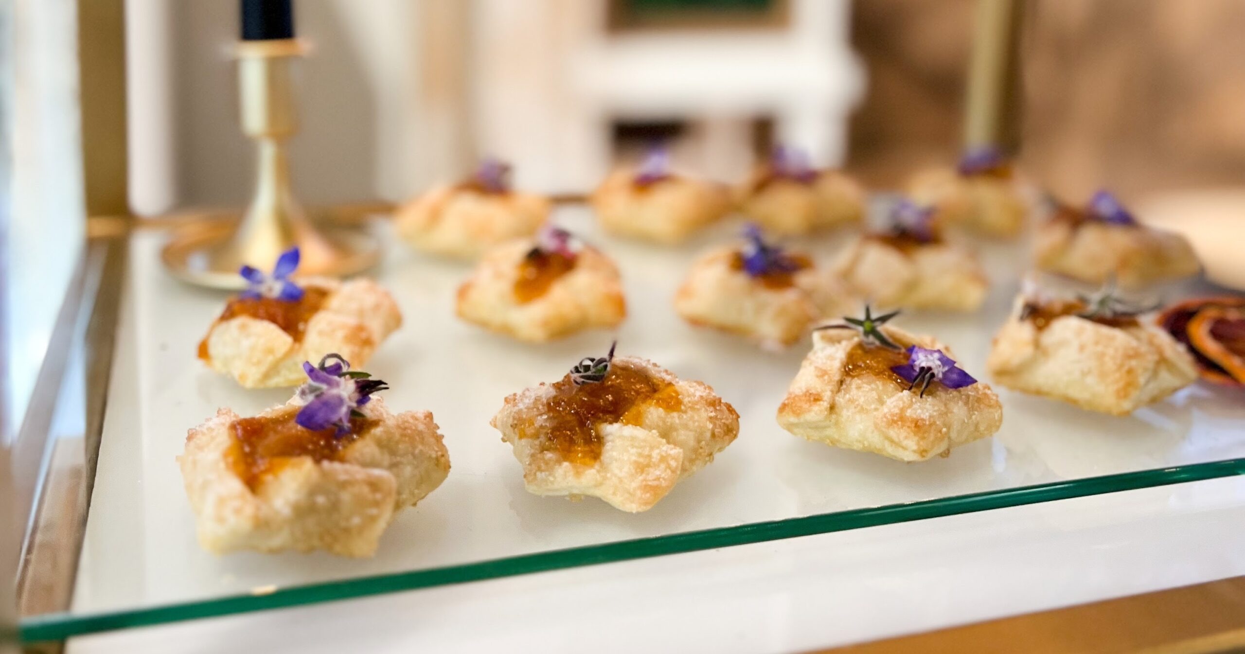 Gourmet canapés with jam and edible flower garnishes arranged on glass platter