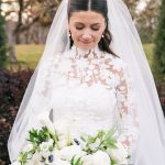 Bride in lace wedding dress and veil holding white bouquet with roses, calla lilies, and anemones