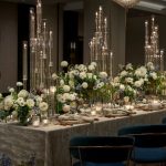 Formal dining table featuring tall glass candelabras and white rose arrangements with navy upholstered seating