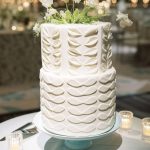 Two-tier white wedding cake with gold scalloped piping detail on turquoise cake stand