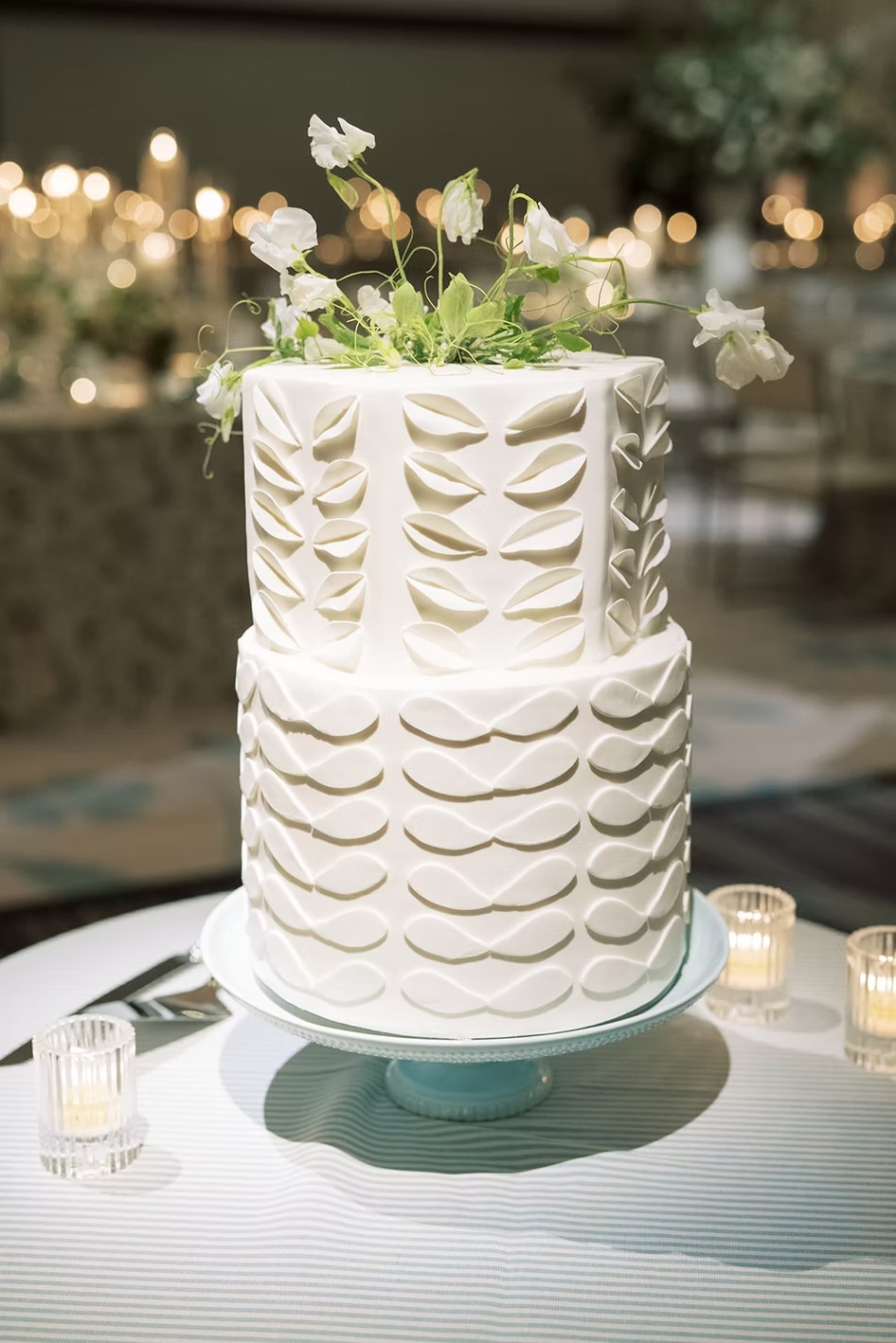 Two-tier white wedding cake with gold scalloped piping detail on turquoise cake stand