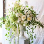 Romantic white wedding floral centerpiece with garden roses and cascading vines in stone urn