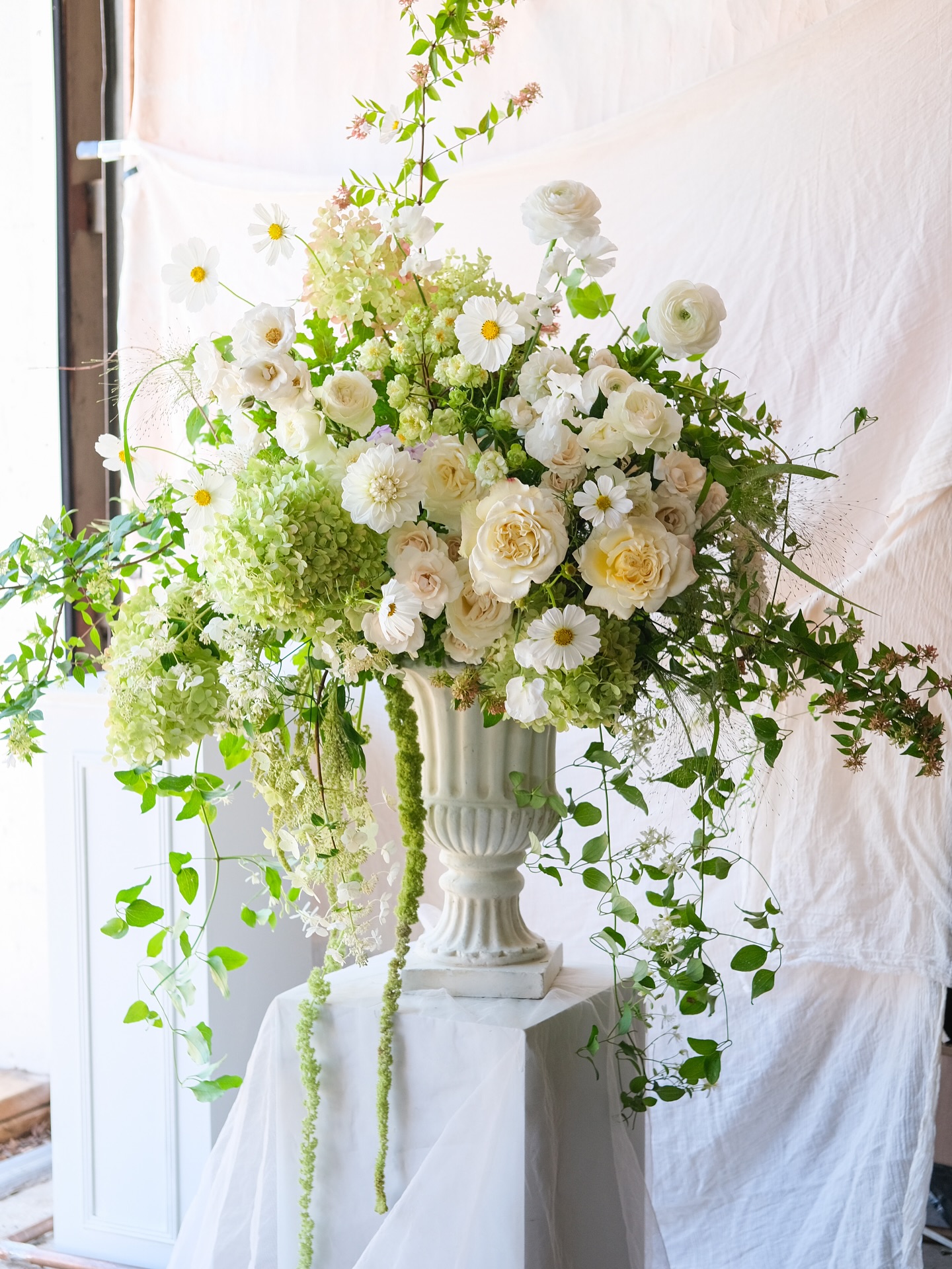 Romantic white wedding floral centerpiece with garden roses and cascading vines in stone urn