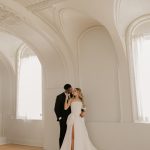 Bride and groom posing in elegant ballroom with ornate white arched architecture and vaulted ceilings