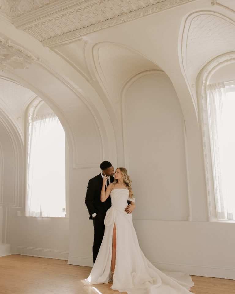 Bride and groom posing in elegant ballroom with ornate white arched architecture and vaulted ceilings