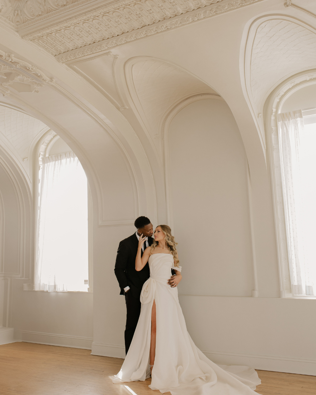 Bride and groom posing in elegant ballroom with ornate white arched architecture and vaulted ceilings
