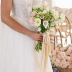 Bride in strapless lace wedding dress holding bouquet of white and pink flowers with silk ribbons
