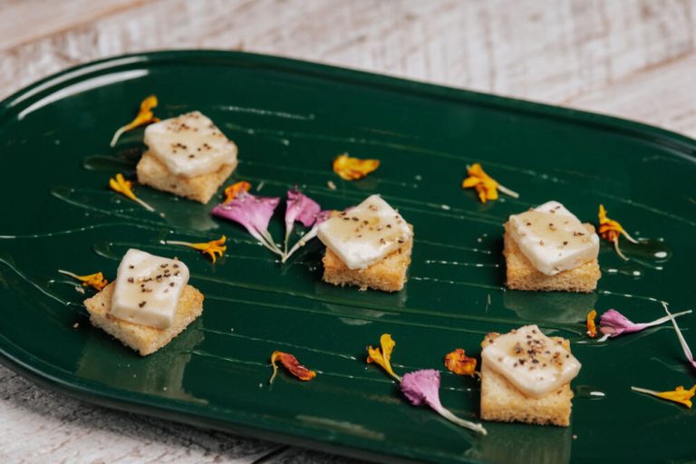 Gourmet canapés with white topping on crispy bread, garnished with edible flowers on green plate