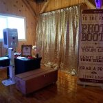 Chaos Productions photo booth setup featuring gold sequin curtain and prop station in rustic wedding venue