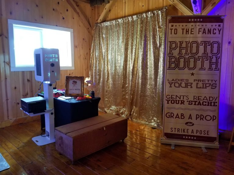 Chaos Productions photo booth setup featuring gold sequin curtain and prop station in rustic wedding venue