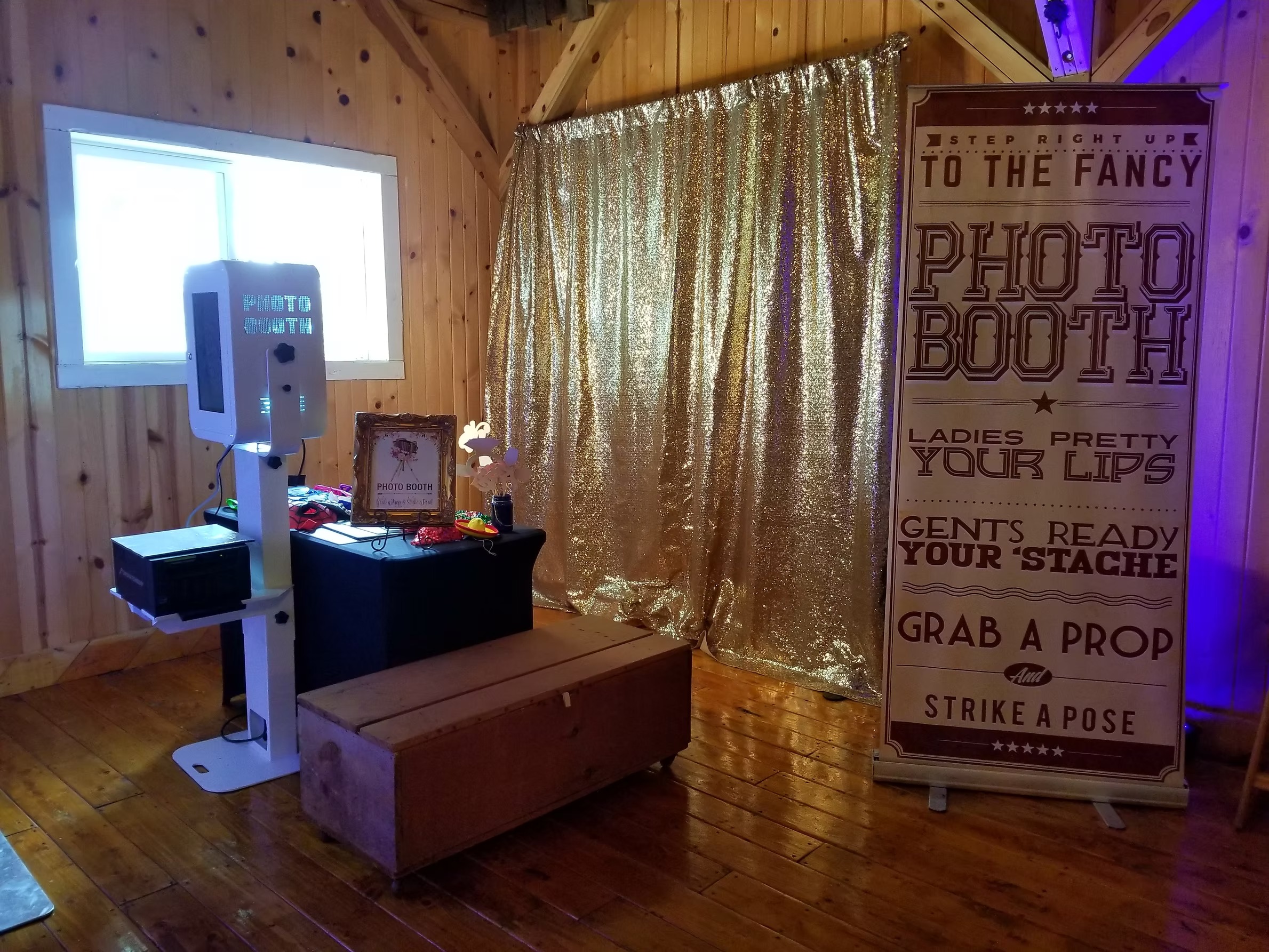 Chaos Productions photo booth setup featuring gold sequin curtain and prop station in rustic wedding venue