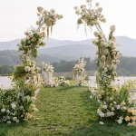 Outdoor wedding ceremony arch adorned with white and cream florals overlooking mountain landscape