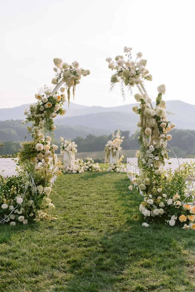 Outdoor wedding ceremony arch adorned with white and cream florals overlooking mountain landscape