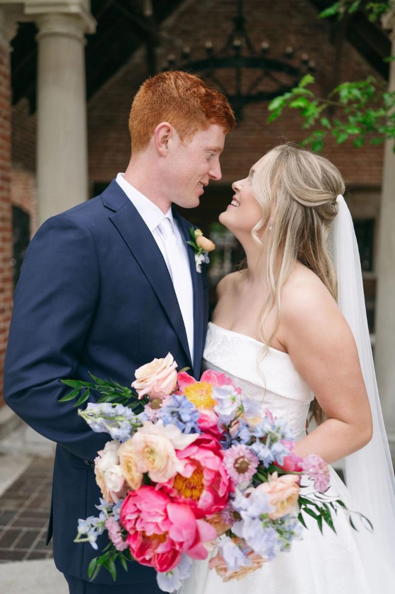 Bride and groom gazing at each other holding vibrant pink and coral peony bouquet at Nebraska wedding venue