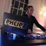 DJ performing at an elegant indoor event with laptop displaying "PHILIP Z" branding and professional mixing equipment